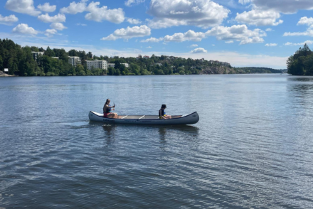 En kanot i vattnet, där en lägerledare och ett barn tillsammans paddlar kanoten.