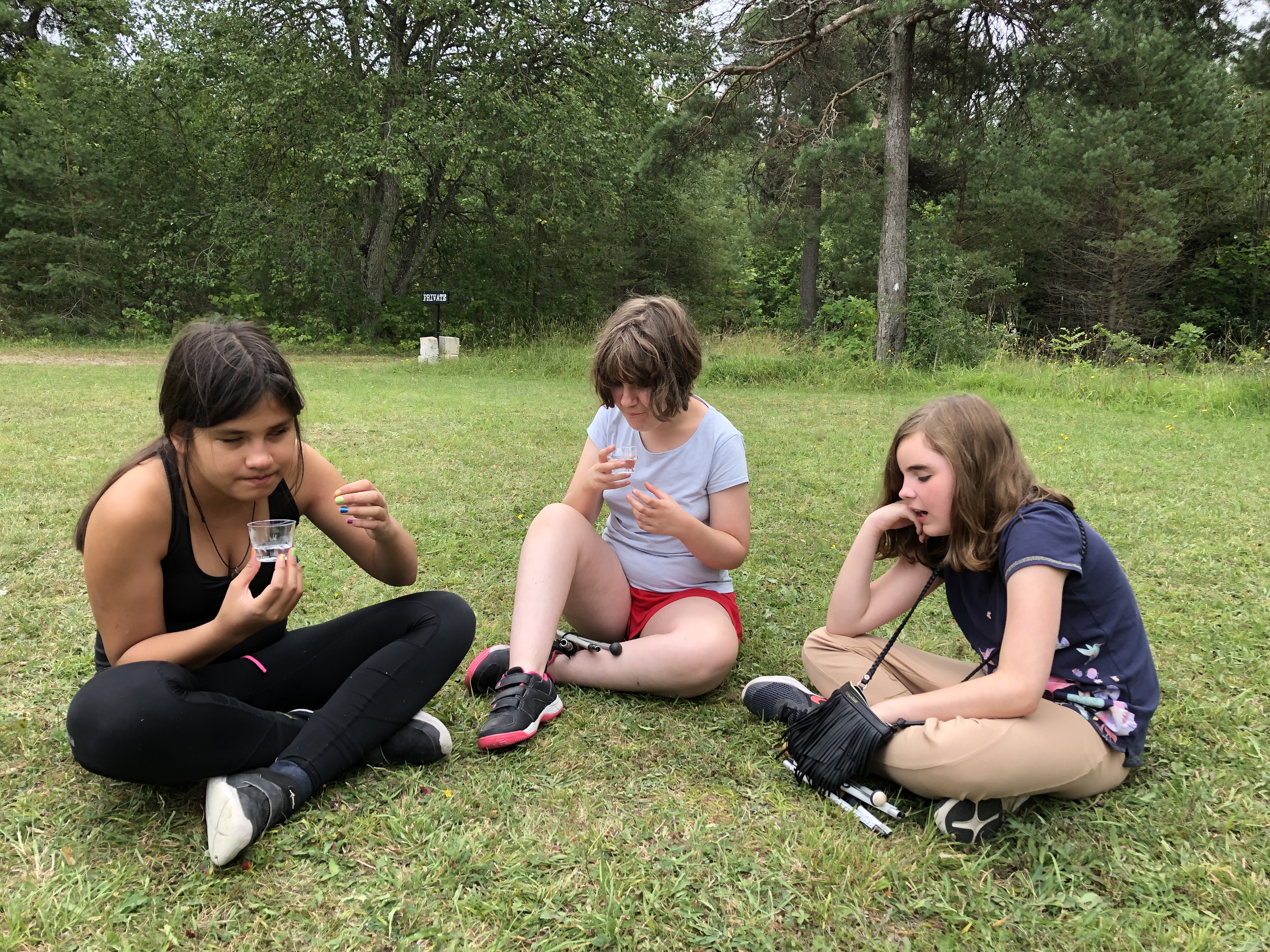 Deltagarna Blanka, Liv och Angelina sitter i skräddarställning på en gräsmatta och pratar.