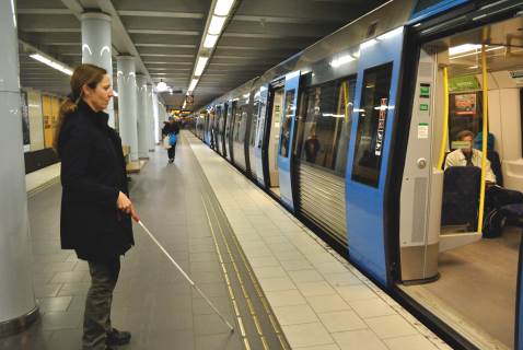 Kvinna med käpp står framför tunnelbanans öppna dörrar